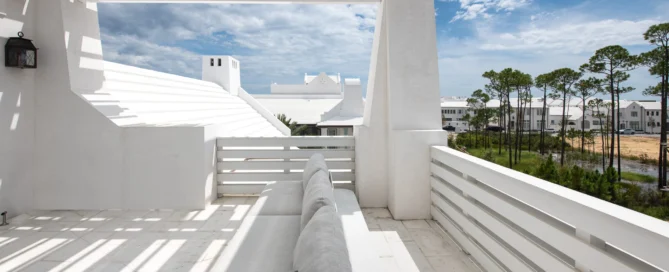 Modern white rooftop patio with a cozy sofa, overlooking Lake Norman townhomes and surrounding trees under a partly cloudy sky.
