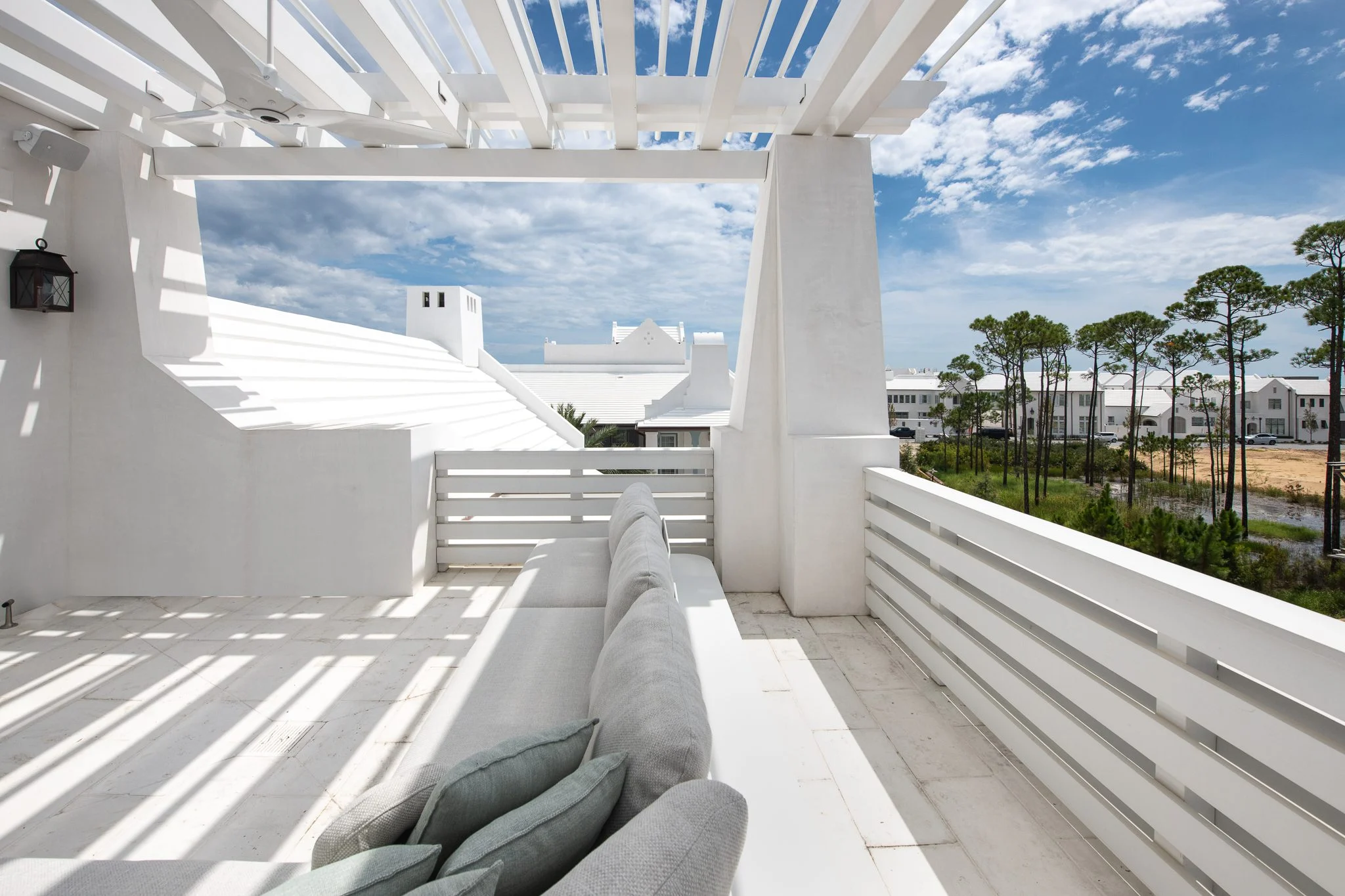 Modern white rooftop patio with a cozy sofa, overlooking Lake Norman townhomes and surrounding trees under a partly cloudy sky.
