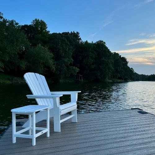 White Adirondack chair and table on a dock overlook a serene lake, surrounded by trees at dusk near Lake Norman townhomes. White Adirondack chair and table on a dock overlook a serene lake, surrounded by trees at dusk near Lake Norman townhomes.
