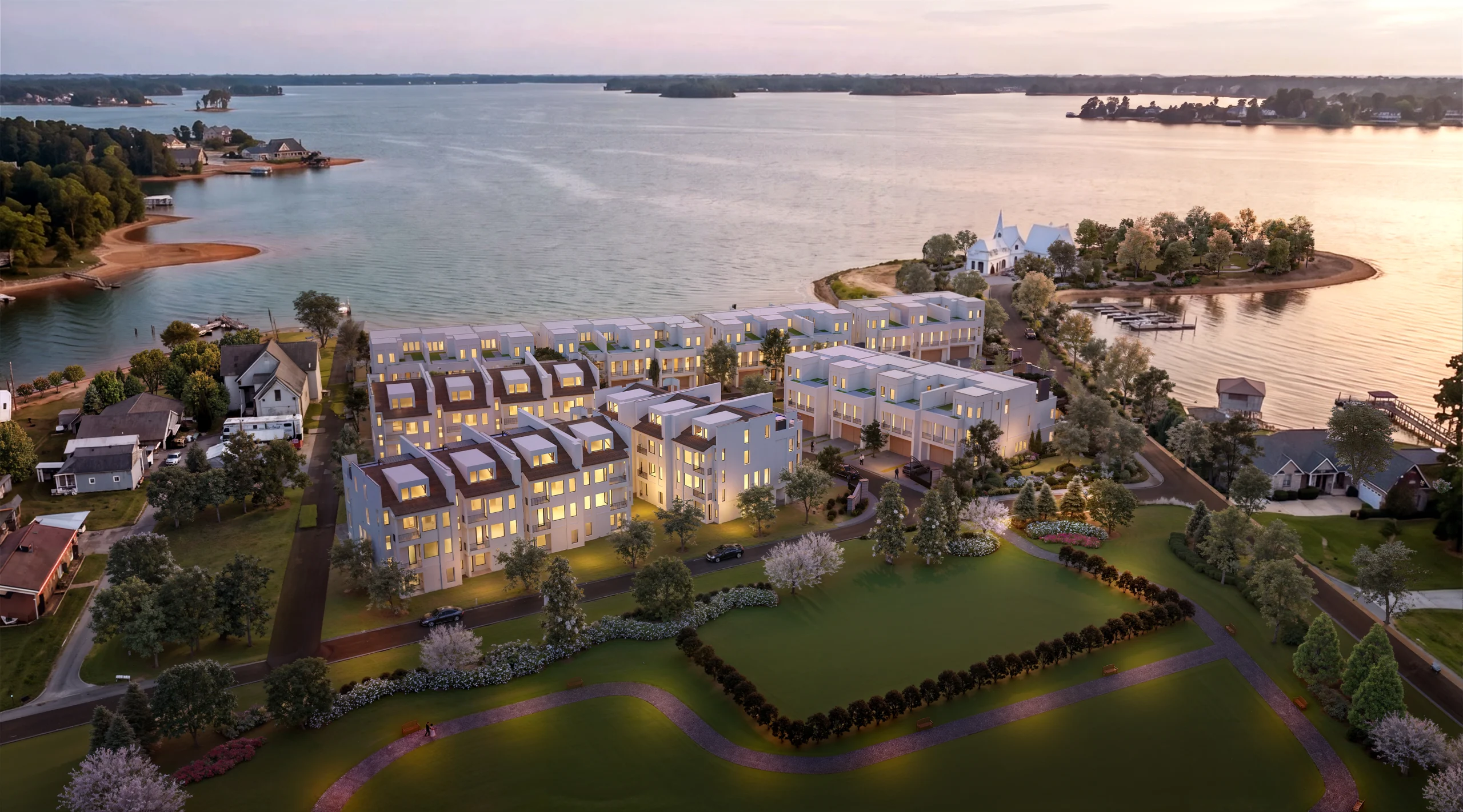 Aerial view of illuminated Lake Norman townhomes at dusk, beside a calm waterfront with tree-lined shores and a small peninsula.