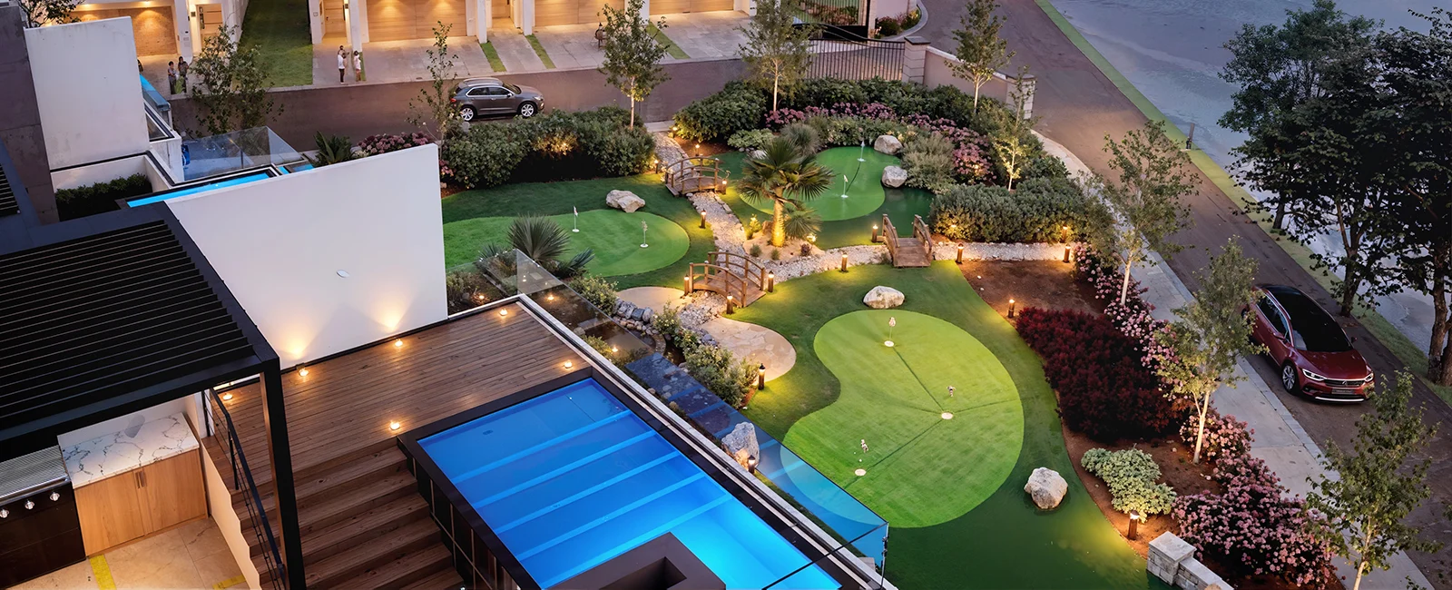 Lake Norman townhomes feature a landscaped garden with mini-golf, illuminated pathways, a pool, and parked cars nearby.