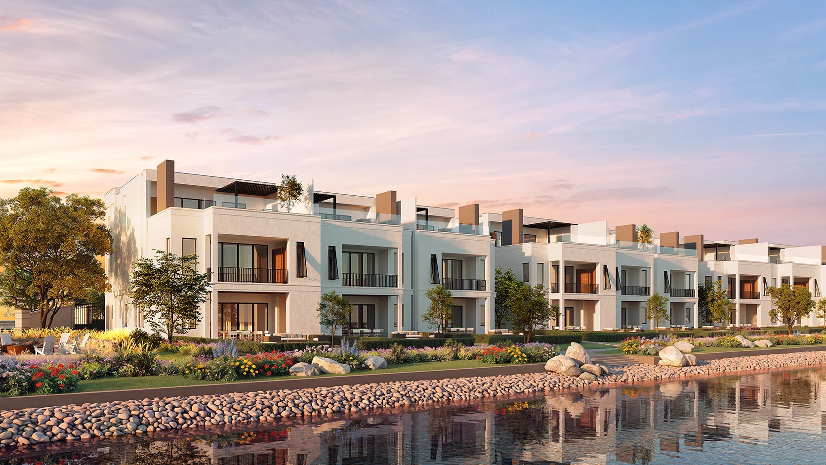 Modern Lake Norman townhomes with large balconies, surrounded by colorful landscaping and a serene waterfront under a pastel sunset sky.